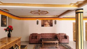 A room with a sofa, a wooden table, a Buddha statue, and a decorative ceiling. - Rabgais Nubra Retreat (Hunder)