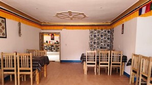 Un espace repas avec des chaises et des tables en bois, un plafond agrémenté d’un luminaire décoratif et un mur orné d’un motif.