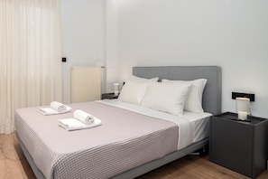 Ein ordentlich bezogenes Bett mit Kissen und Handtüchern, ein Nachttisch mit Lampe und ein Heizkörper an der Wand.