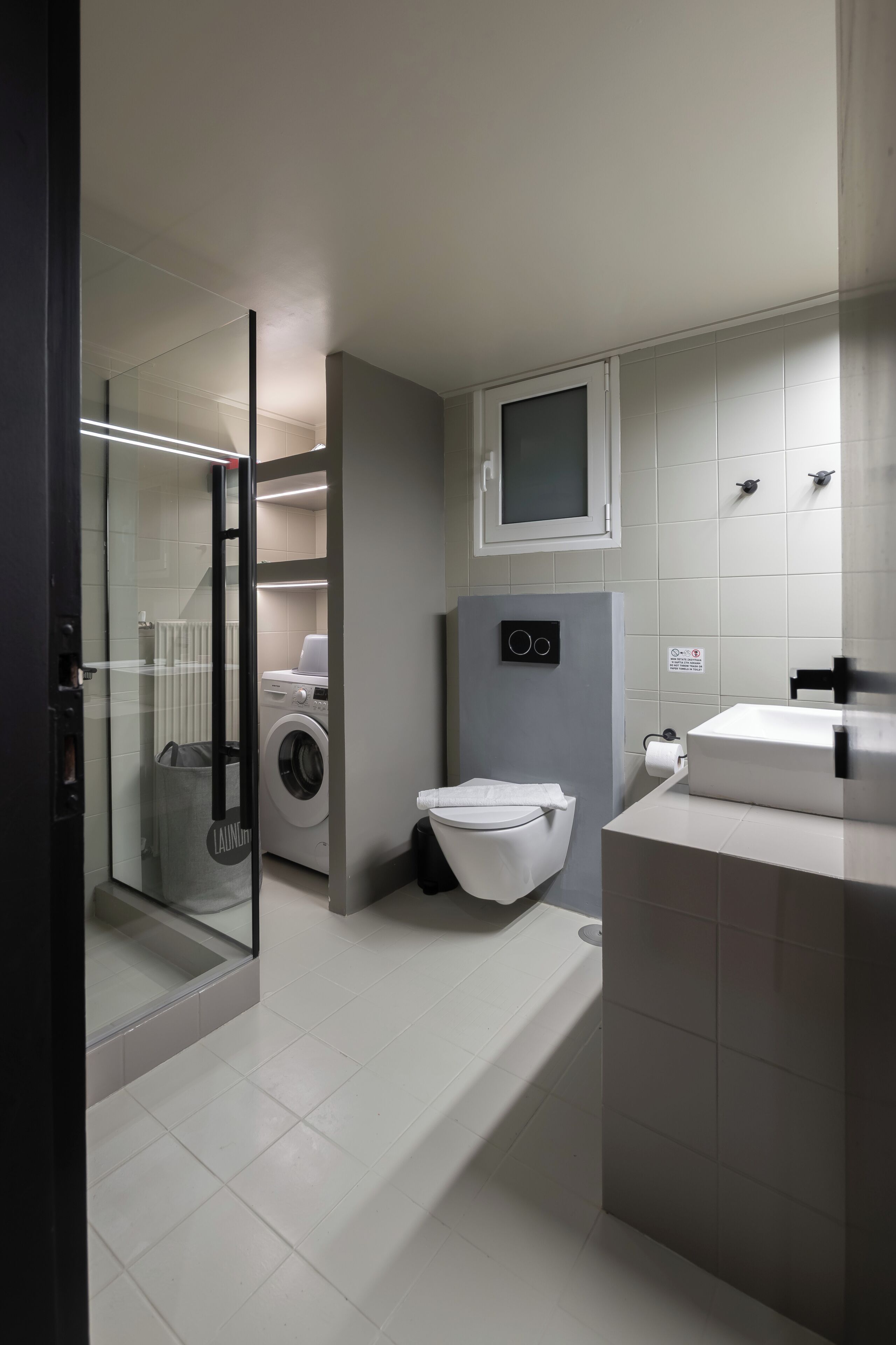 Een moderne badkamer met een douchecabine van glas, een wasmachine, een toilet en een wastafel.