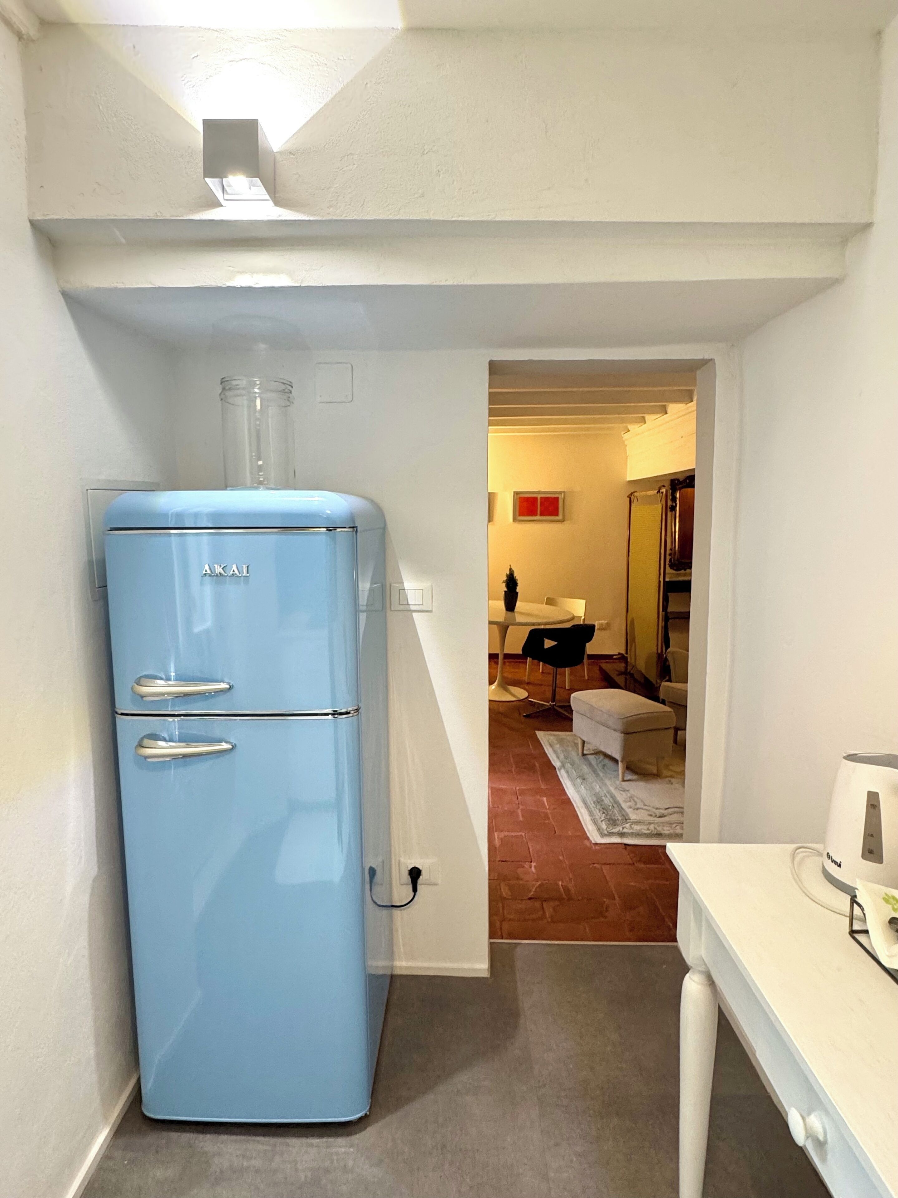 A compact kitchen with a blue refrigerator, a white countertop, and a visible doorway leading to a dining area.
