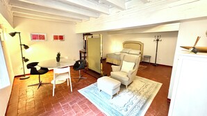 A spacious room with a bed, a chair, a table, and a floor lamp. - Santo Spirito Cute Loft (Firenze)