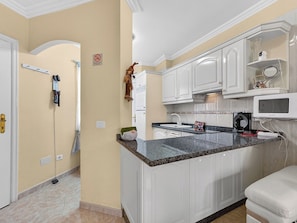A kitchen with white cabinets, a granite countertop, a microwave, and a small seating area. - Kris Costasol by Interhome (Costa del Silencio)