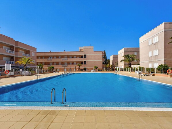 Una piscina con solárium de baldosas, rodeada de edificios de varios pisos con balcones.