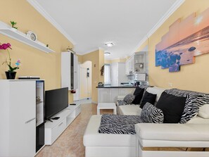 A modern living room with a flat-screen TV, a sofa with zebra print cushions, a kitchen area with white cabinets, and a dining table. - Kris Costasol by Interhome (Costa del Silencio)