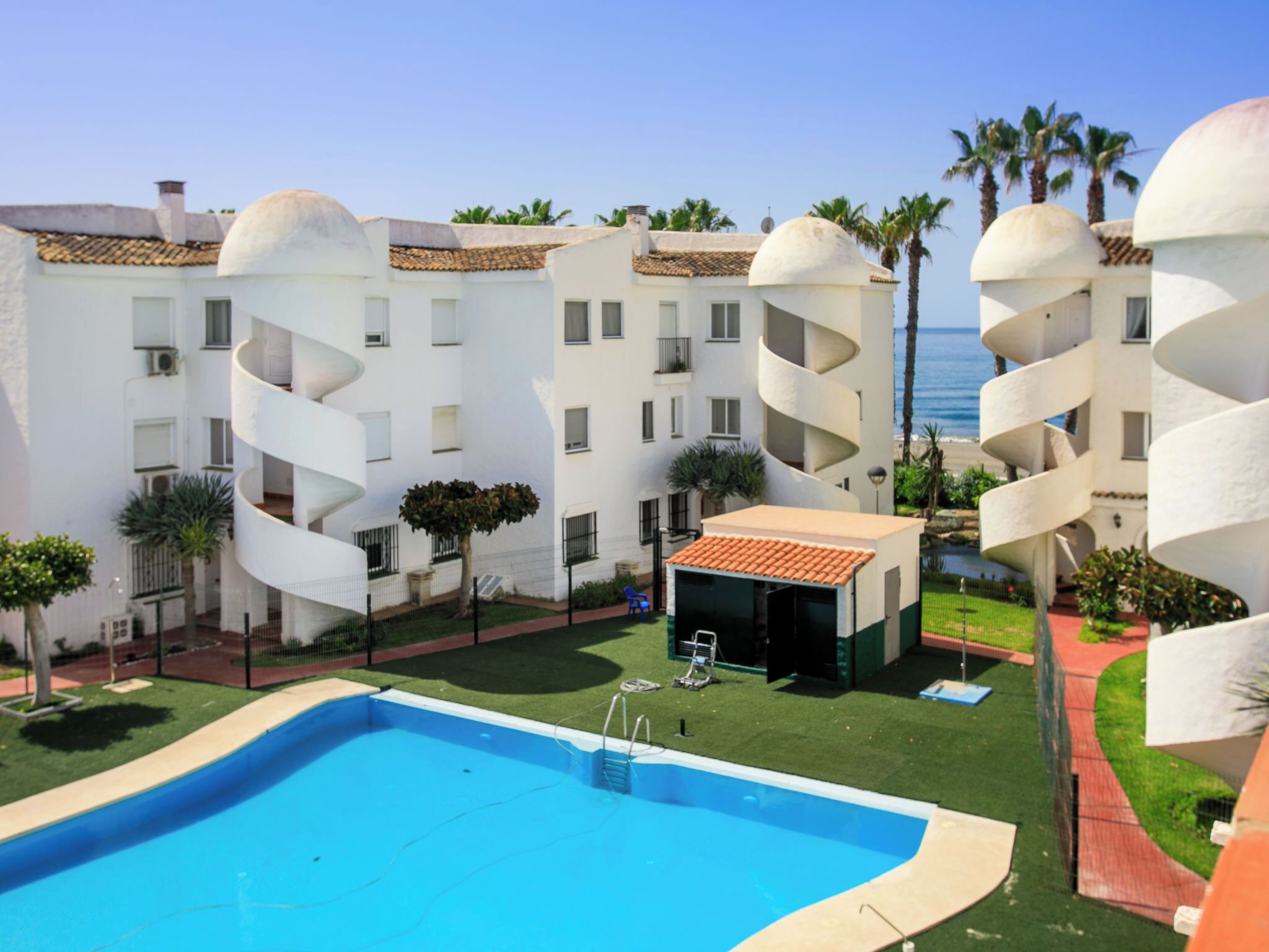 A pool area with a clear view of a building with spiral balconies and a small pool house.