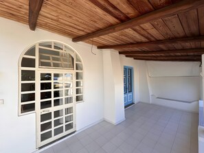 A room with a tiled floor, a large arched window, a blue door, and wooden ceiling beams.