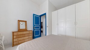 A bedroom with a bed, a dresser, a wardrobe, and a door leading to another room.
