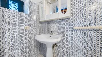 Ein Badezimmer mit einem weißen Waschbecken, blauen Fliesen mit Muster, einem Spiegel und einem Fenster mit geometrischem Design.
