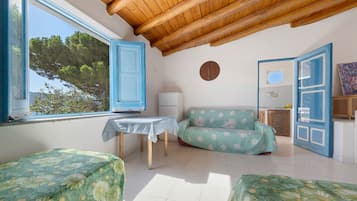 Una stanza con soffitto in legno, un divano con motivo floreale, un tavolo con tovaglia bianca e una finestra vista alberi.