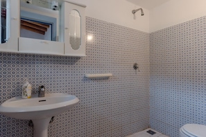 A bathroom with a white pedestal sink, a mirror above it, and patterned tiles on the walls. - Apartment 'Quadara - Sul Rifugio' with Sea View, Private Terrace and Shared Garden (Lingua)