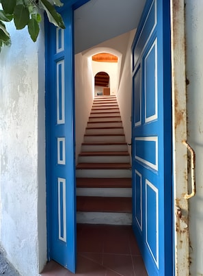 Eine Treppe führt zu einem Raum mit Holzbalkendecke, blauen Türen und einer weißen Wand.