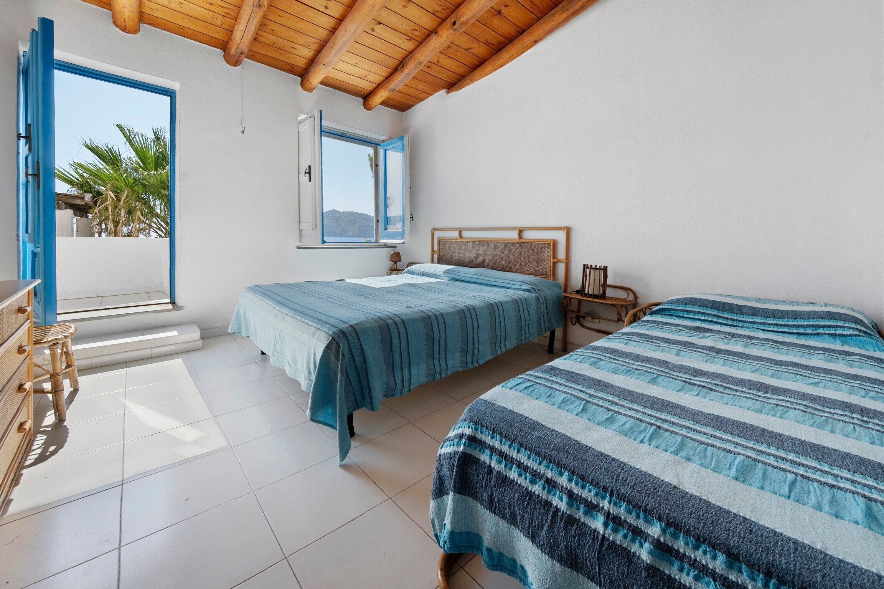 A bedroom with two beds, a window with a view, and a wooden ceiling.