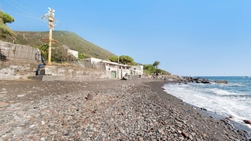 Una playa de guijarros con un edificio y un molino de viento al fondo.