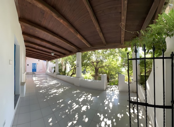 Un espacio exterior techado con piso de baldosas, vigas de madera en el techo y vista a la vegetación.