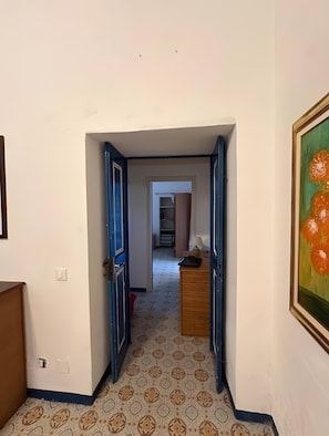 A hallway with patterned floor tiles, a wooden dresser, and a painting of oranges.