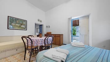 Una stanza con un letto, un tavolo con sedie, un quadro appeso al muro e una porta che dà sull'esterno.