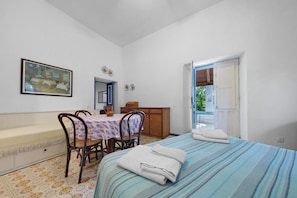 Una habitación con cama, una mesa y sillas, un cuadro en la pared y una puerta que da al exterior.