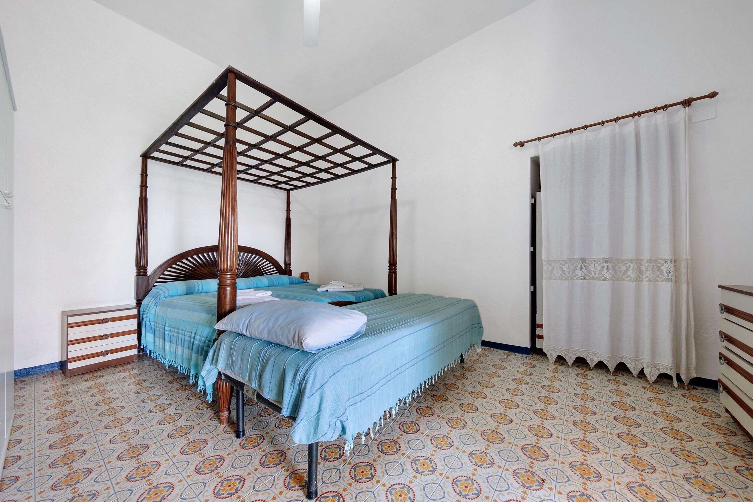 A four-poster bed with a wooden frame, a matching nightstand, and a patterned floor.