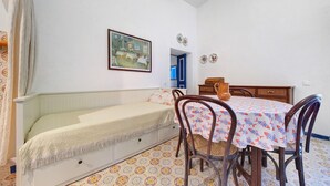 A room with a bed, a dining table with chairs, a painting on the wall, and a patterned floor.