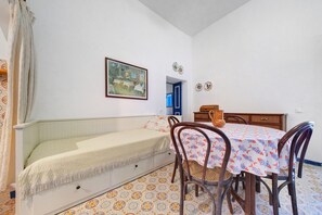 A room with a bed, a dining table with chairs, a painting on the wall, and a patterned floor.