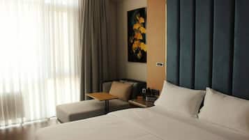 Habitación de hotel con cama, escritorio, silla, un cuadro y ventana con cortinas.