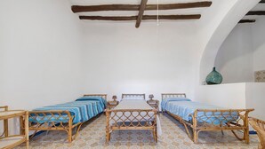 A room with four wooden beds arranged in a row, a tiled floor with a geometric pattern, and a white wall with a wooden beam ceiling.