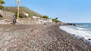 A pebbled beach with a building and a windmill in the background.
