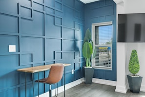 A room with a blue wall, a wooden table, a brown chair, a potted plant, and a TV on the wall. - Hyde Park Deluxe private residence (Tampa)