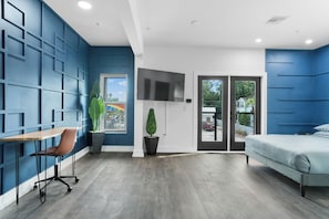 Een moderne kamer met een blauwe accentmuur, een flatscreen televisie, een bed, een bureau met stoel en een potplant.