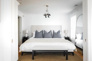 A bedroom with a large bed, bedside tables, a chandelier, and a view of the outside.