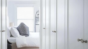 Un dormitorio con una cama, un armario blanco, suelo de madera y una ventana con persianas.