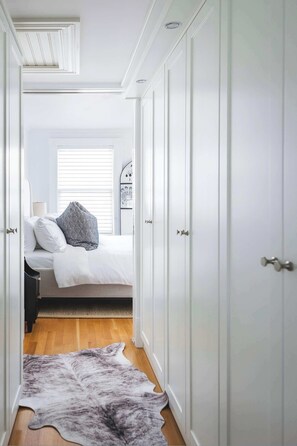 A bedroom with a bed, a white wardrobe, a wooden floor, and a window with blinds.