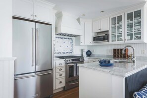 A modern kitchen with white cabinetry, stainless steel appliances, and a marble countertop.