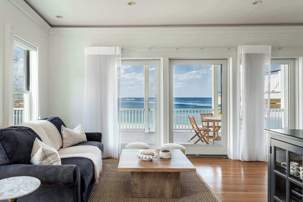 A living room with a dark-colored sofa, a wooden coffee table, and a view of the ocean through large windows.