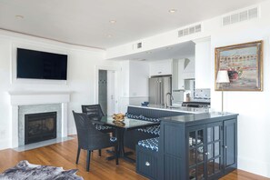 A modern kitchen with a central island, a dining area with chairs, a fireplace, and a mounted TV.