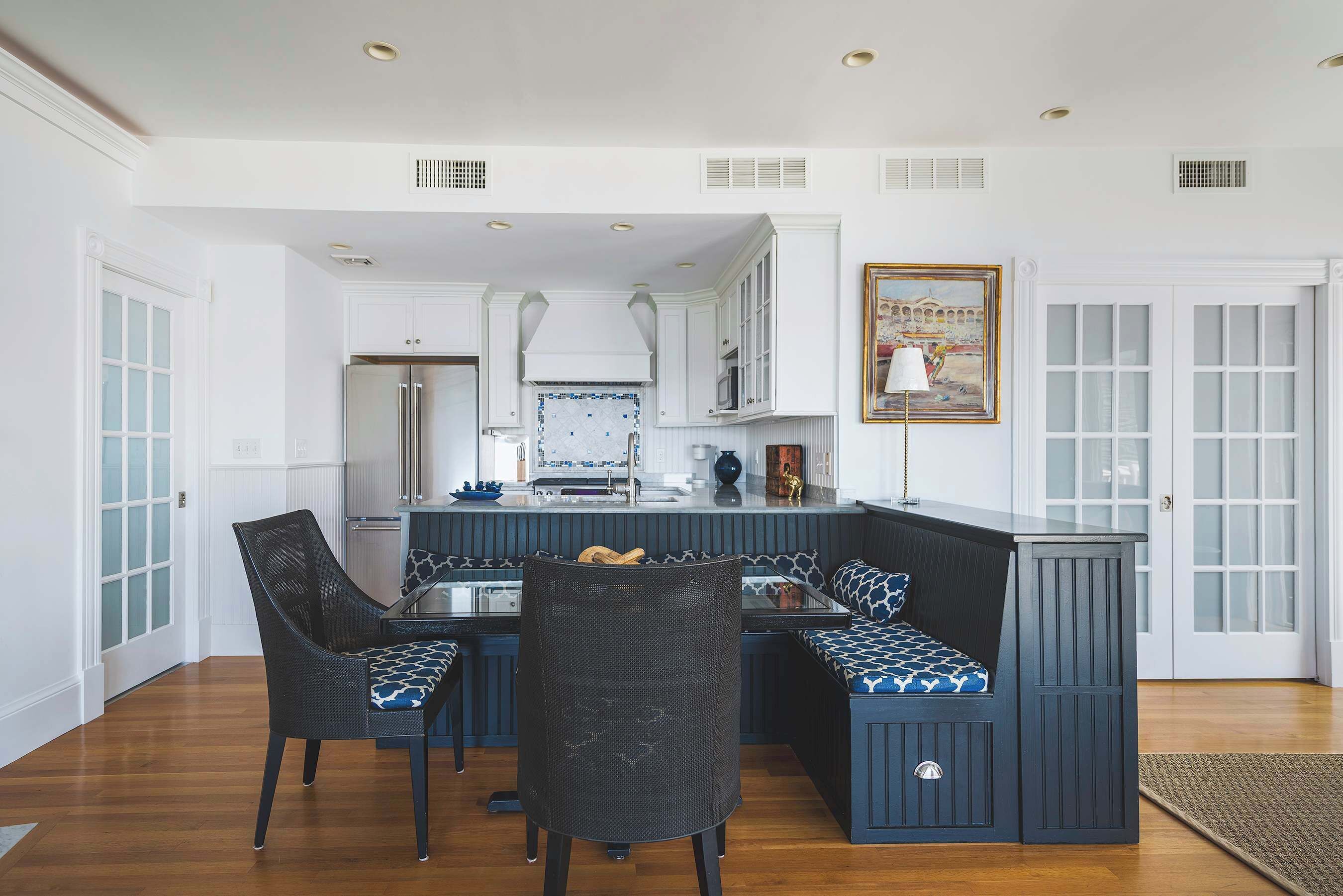 A kitchen with white cabinetry, a central island with seating, and a dining area with chairs.