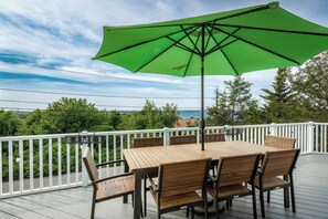 Una terraza de madera con una mesa, sillas, un parasol verde y una barandilla blanca.