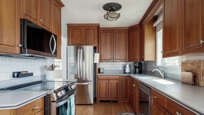 A kitchen with wooden cabinets, stainless steel appliances, a microwave, and a refrigerator. - Stay at Wingaersheek (Gloucester)
