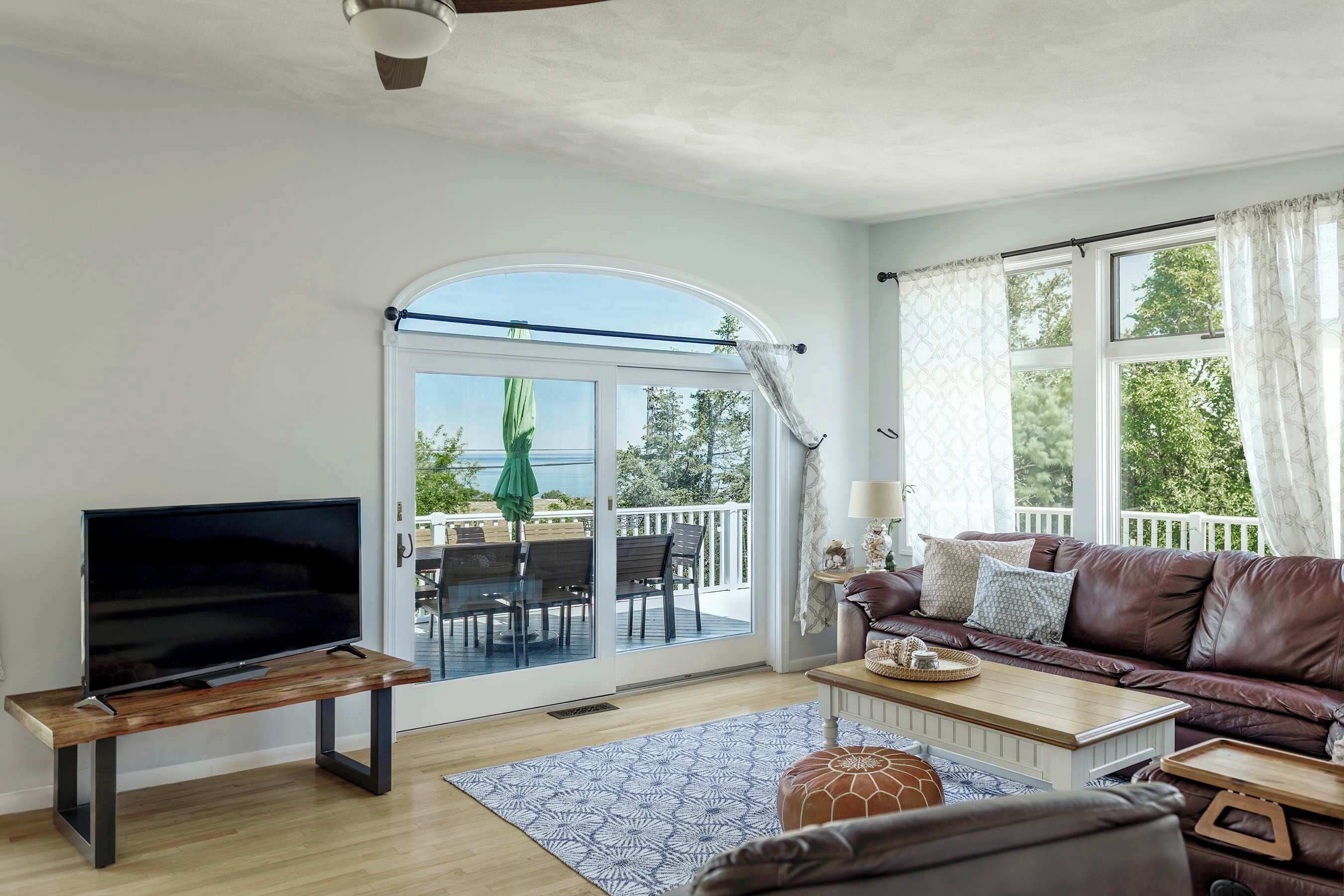 A living room with a TV on a wooden stand, a brown leather sofa, a coffee table, and a patterned rug.