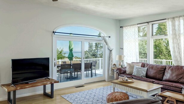 A living room with a TV on a wooden stand, a brown leather sofa, a coffee table, and a patterned rug. - Stay at Wingaersheek (Gloucester)