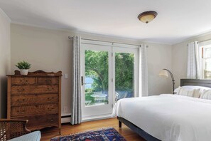 Un dormitorio con cama, cómoda, lámpara y vista a través de un ventanal corredero.