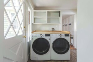 Una sala de lavandería con dos lavadoras de carga frontal, una encimera de madera y un estante blanco.