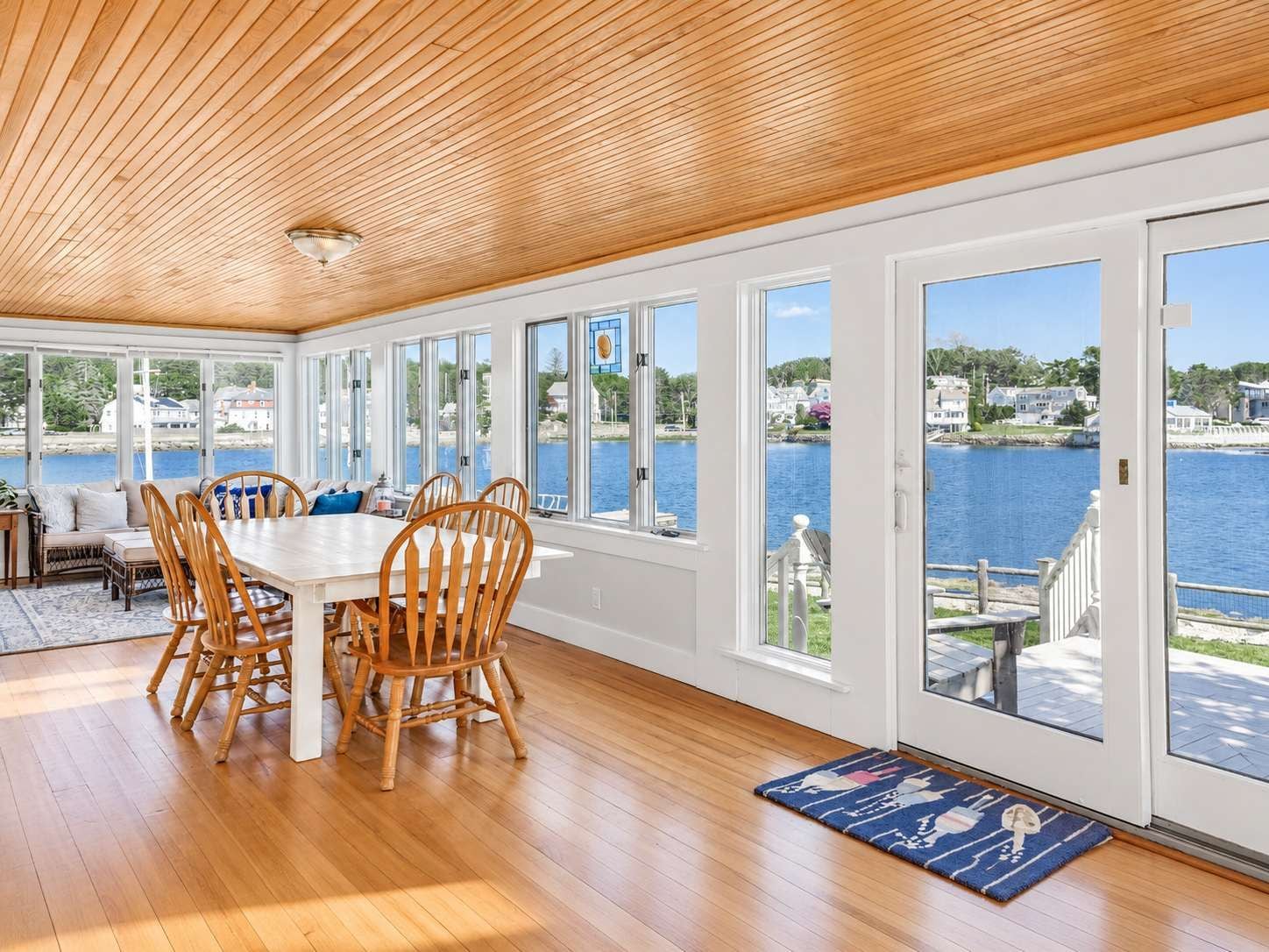A spacious room with a large dining table, wooden chairs, and a view of a lake through large windows.