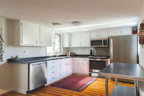 A modern kitchen with white cabinets, stainless steel appliances, and a wooden floor.