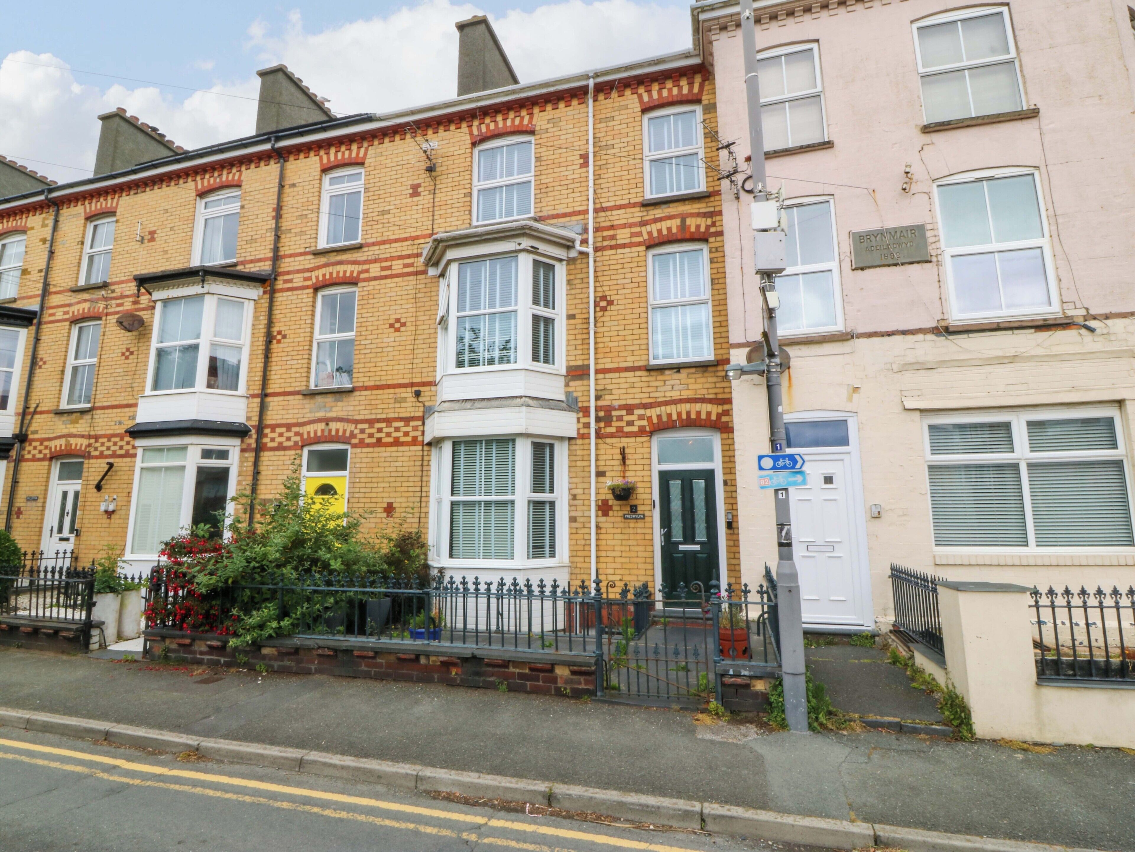 A row of terraced houses with a clear road in front, a blue sign indicating a cycle path, and a yellow flower box on the left.