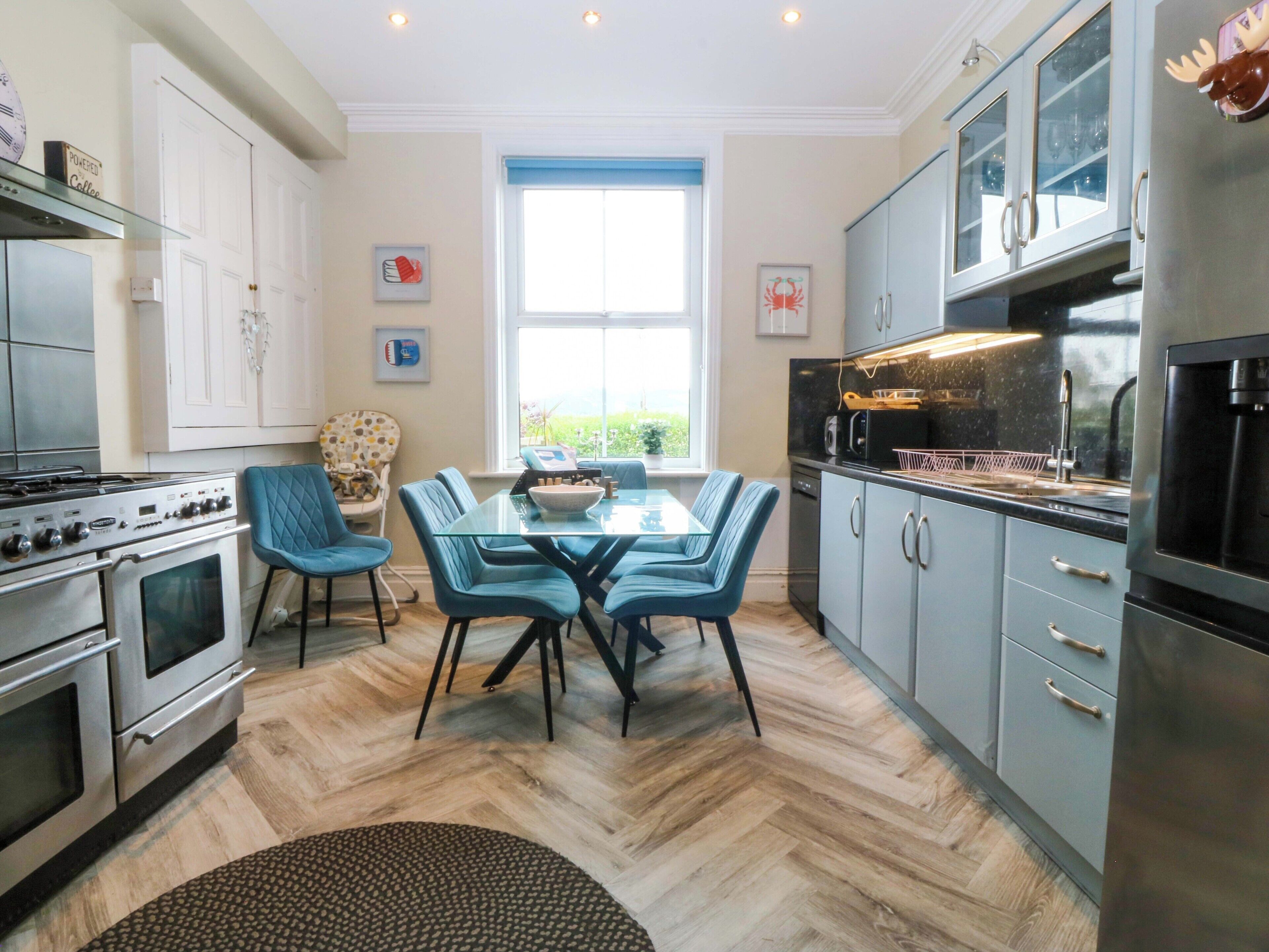 A modern kitchen with a dining area, featuring a large window, stainless steel appliances, and blue chairs.