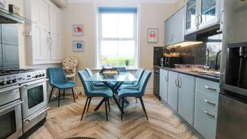 A modern kitchen with a dining area, featuring a large window, stainless steel appliances, and blue chairs.