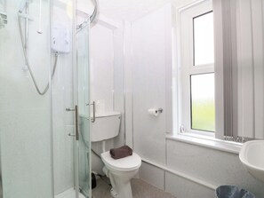 A bathroom with a glass-enclosed shower, a toilet, a window, and a sink. - Jack's House (Tywyn)