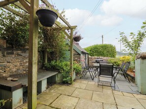 A patio with stone flooring, a wooden pergola, a hanging flower pot, and a stone wall. - Jack's House (Tywyn)